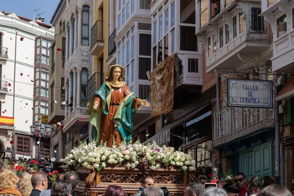 La Virgen con su manto verde y azul entre flores blancas por la calle comercial